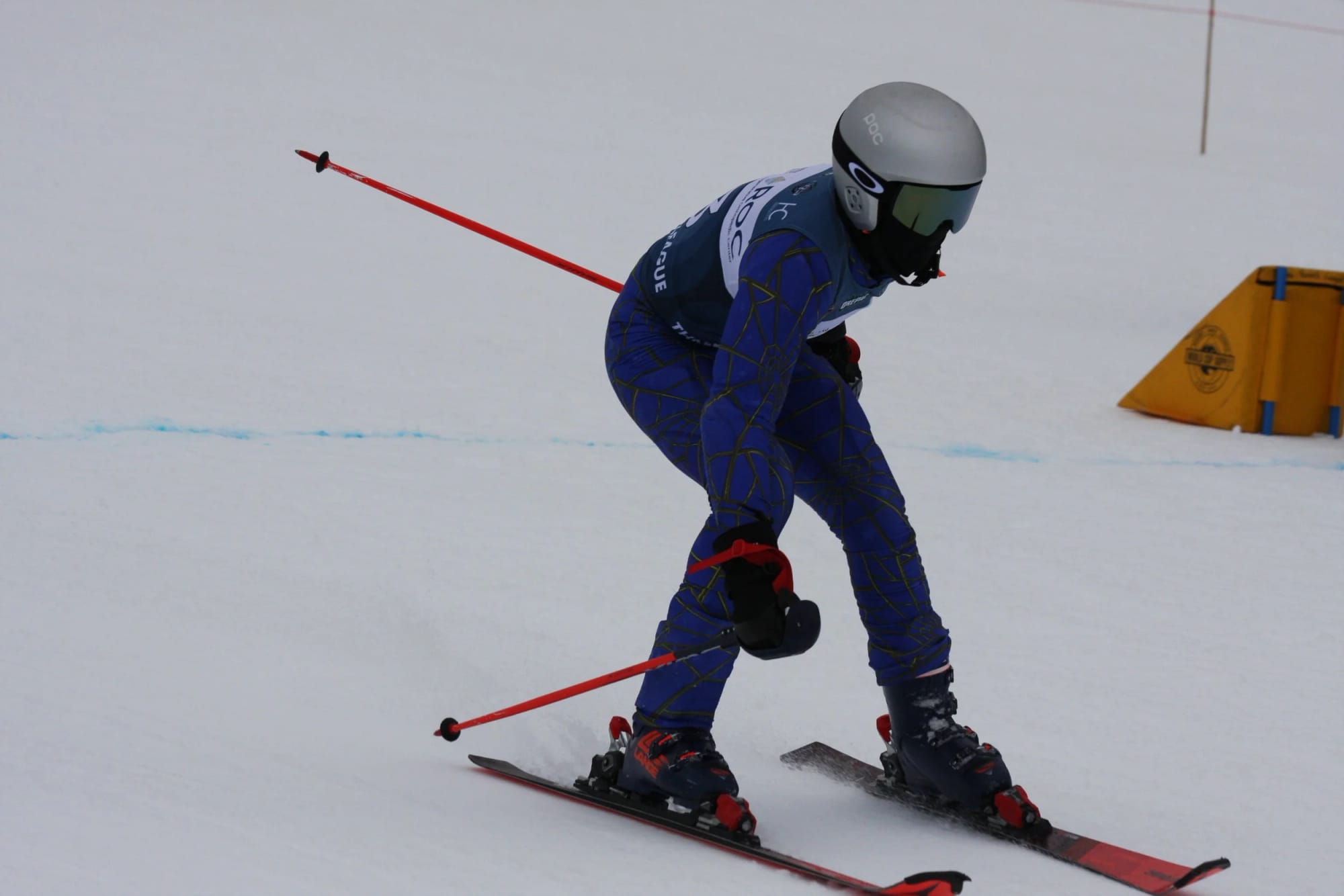 An IBW racer in a low tuck coming out of a giant slalom turn past a red gate