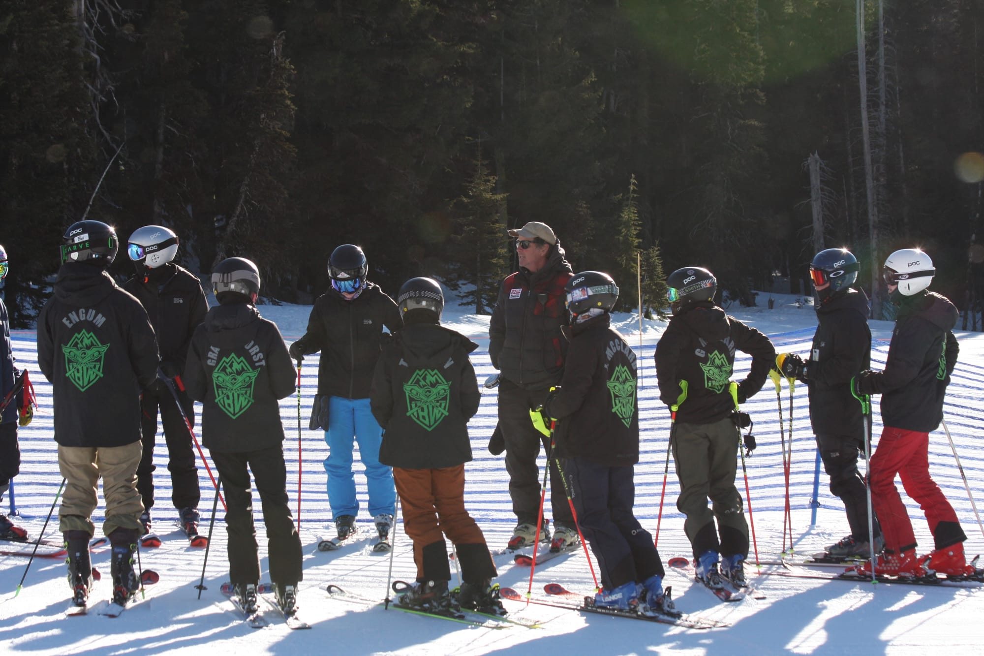 The team lined up along the course fence, Guardians crests across their backs, coach talking them through the line